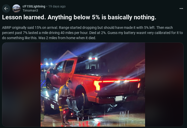 A red Ford F-150 Lightning truck is parked on a wet street with a person inspecting it, highlighting the challenge of low battery levels.