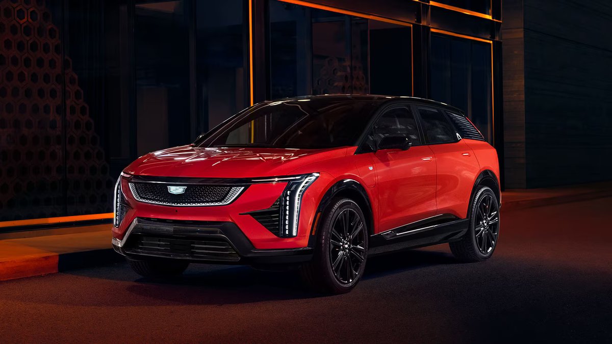 A Red 2025 Cadillac Optiq SUV parked in an urban setting, showcasing modern design with bold lines and a distinctive front grille.