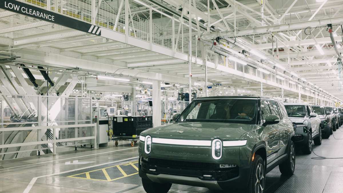 A Rivian R1S in a bright manufacturing facility, lined with other vehicles, showcasing modern assembly operations.
