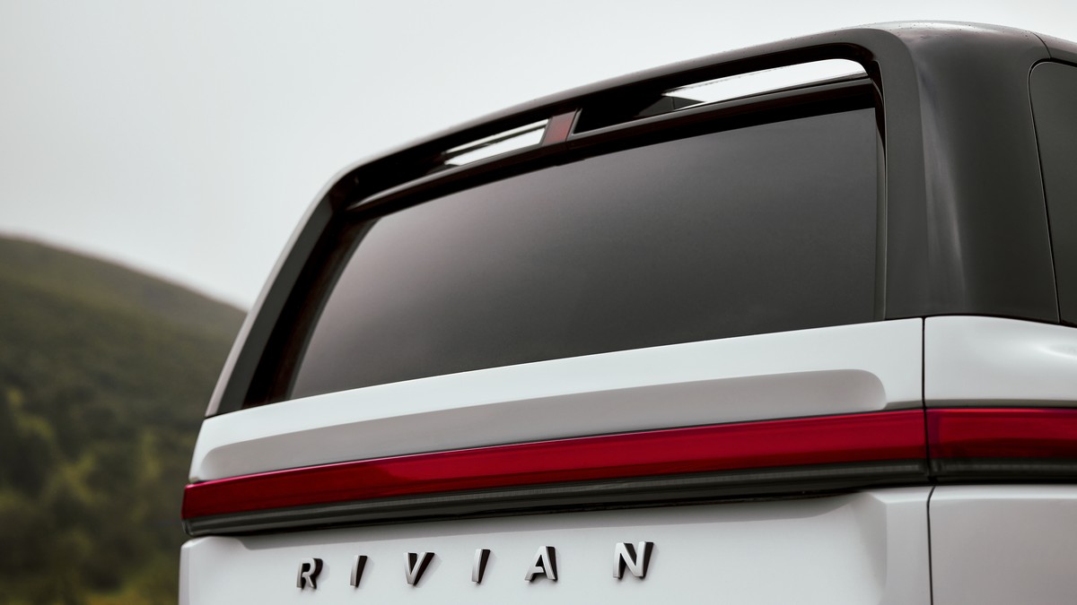 Close-up of a white Rivian vehicle's rear, showcasing sleek design, tinted glass, and the distinctive brand logo below the taillight.