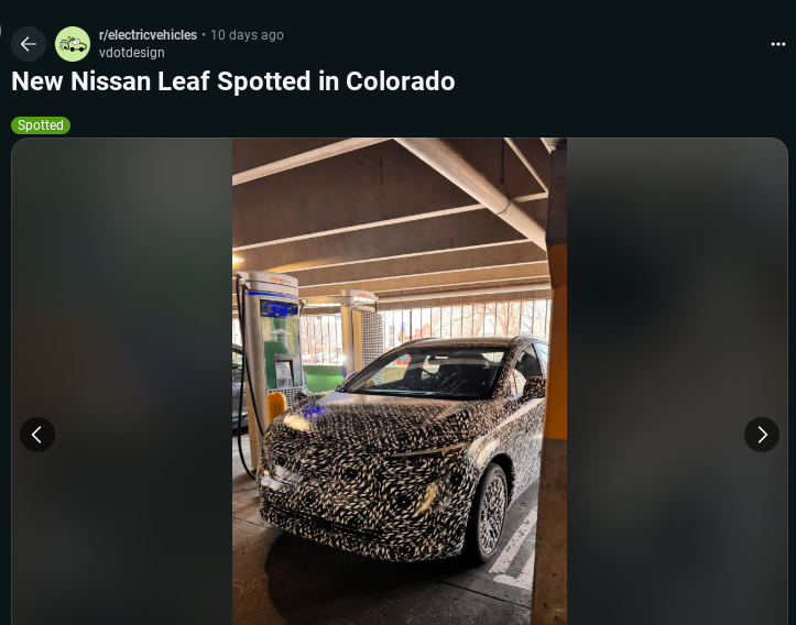A camouflaged new Nissan Leaf parked at a charging station in a Colorado garage, showcasing its futuristic design.
