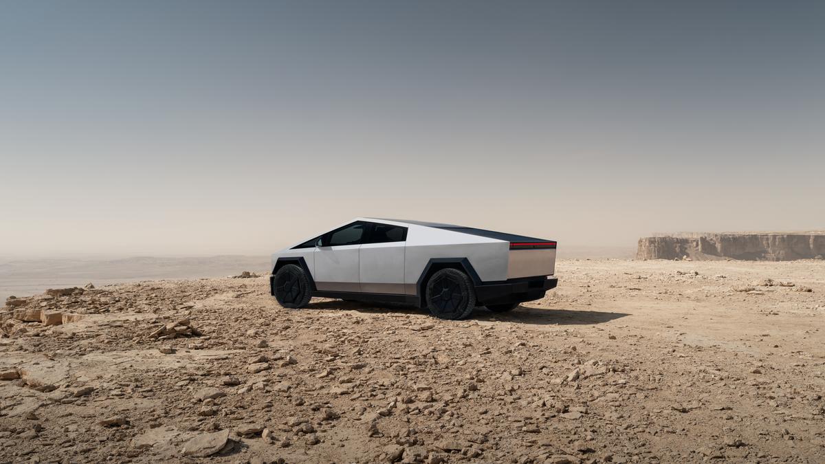A Tesla Cybertruck parked on rocky terrain under a clear sky, showcasing its angular, futuristic design.