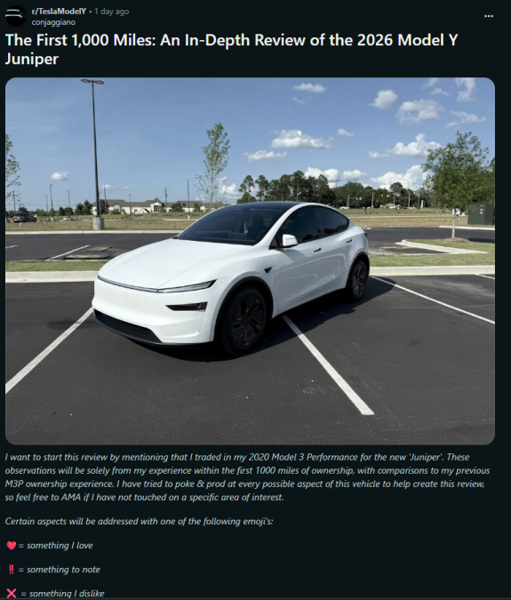 A white 2026 Tesla Model Y Juniper parked on a pavement, surrounded by greenery under a partly cloudy sky.