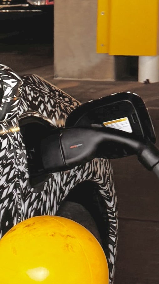 A close-up of a 2026 Nissan Leaf car's side mirror and charging port, next to a parking structure.