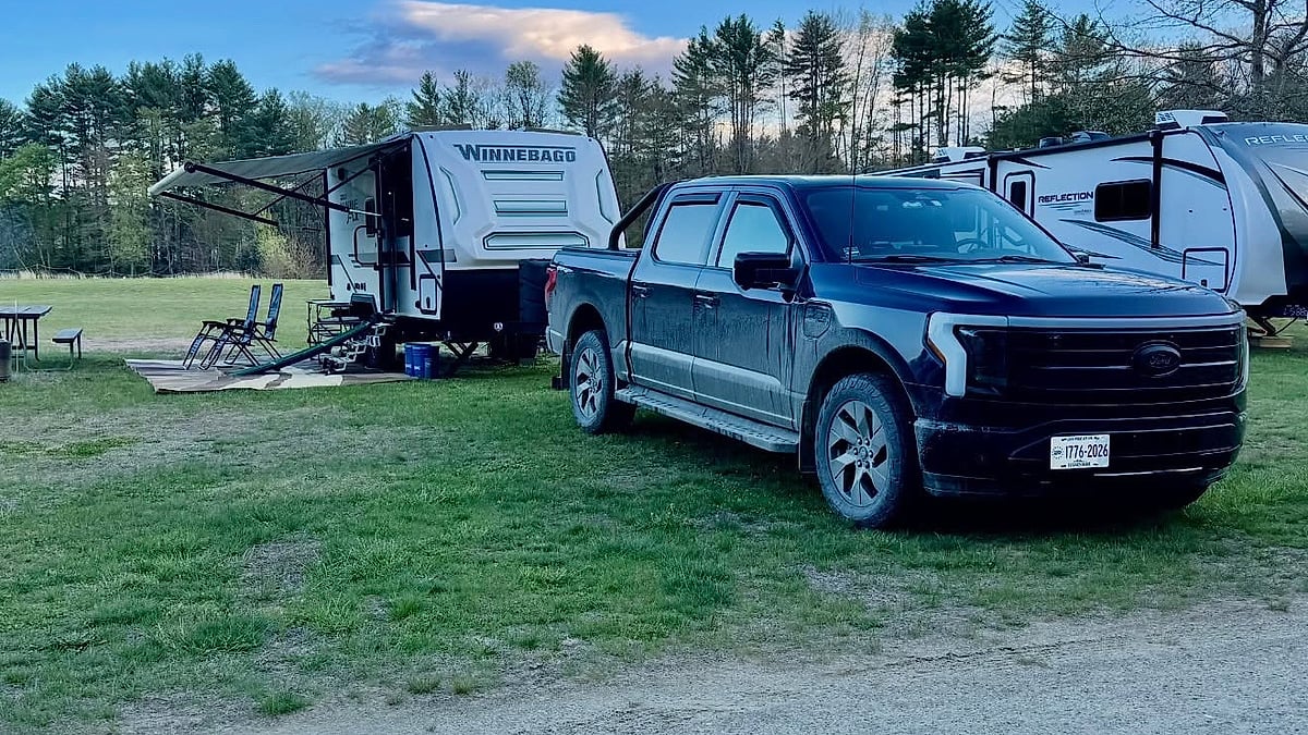 Ford F-150 Lightning parked at a campsite while towing a Winnebago camper trailer with the awning extended.