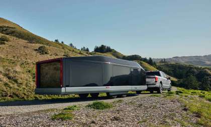 Image of the Lightship L1 camper being towed behind a Ford F150 on a dirt road with green rolling hills surrounding.