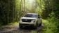 A white Ford Maverick navigates a wooded dirt road