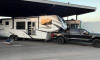 2024 Ford F-250 Super-Duty, Front 3_4 Quarters, Black White Grand Design Solitude luxury fifth-wheel RV parked under covered parking, with black F-250 Powerstroke towing it.